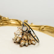 A Black Cuff on a shell on a white background with a gold frame. 