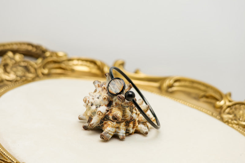 A Black Cuff on a shell on a white background with a gold frame. 