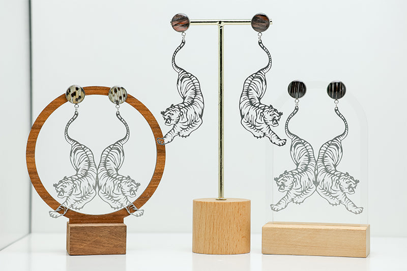 Three pairs of Tiger Earrings on stands on a white background. 