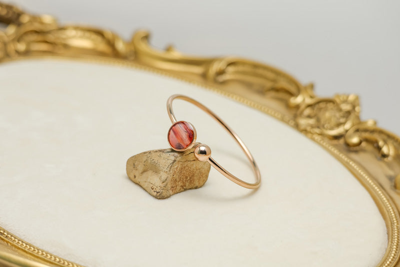 A Rose Gold Cuff on a rock on a white background with gold frame.