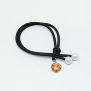 Black hair tie with two pearls and a lionfish charm at the ends on a white background.