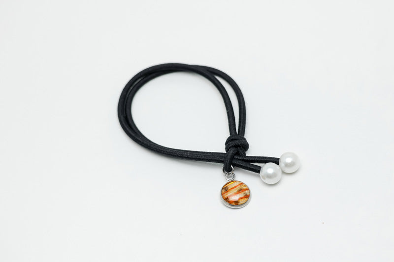 Black hair tie with two pearls and a lionfish charm at the ends on a white background.