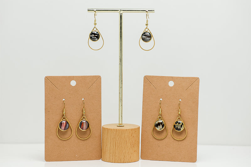 Three pairs of Small Golden Teardrop Earrings on stands on a white background.  