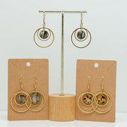 Three pairs of Gold Double Loop Earrings on stands on a white background. 