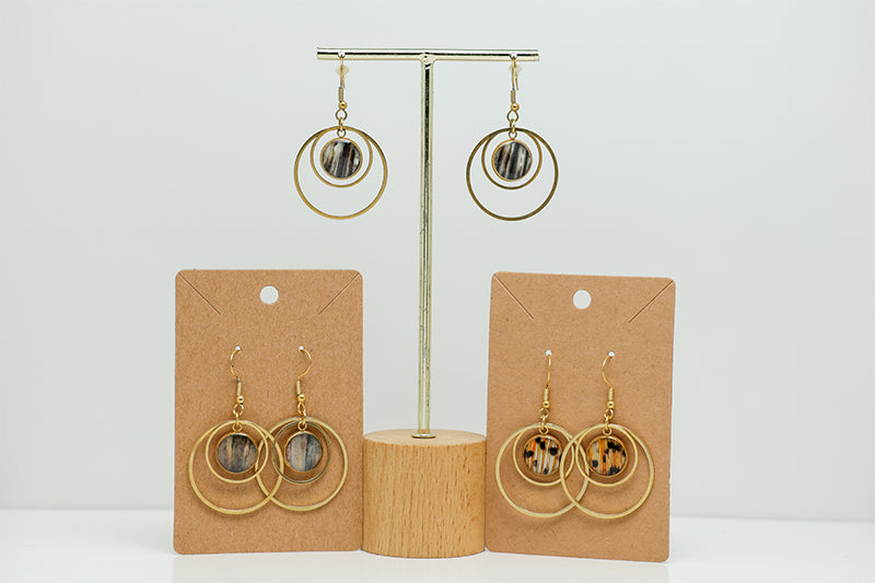 Three pairs of Gold Double Loop Earrings on stands on a white background. 