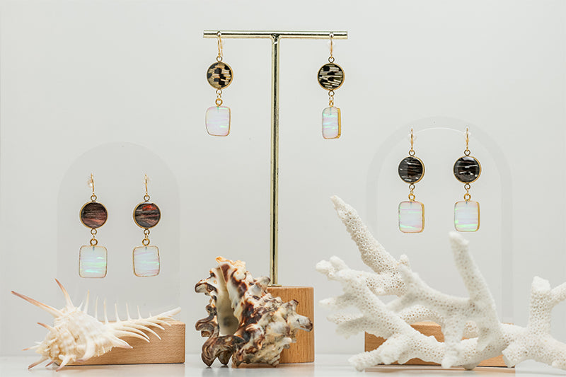 Three pairs of Opal Slice Earrings stands on a white background with two shells and white coral at the bottom of the image. 