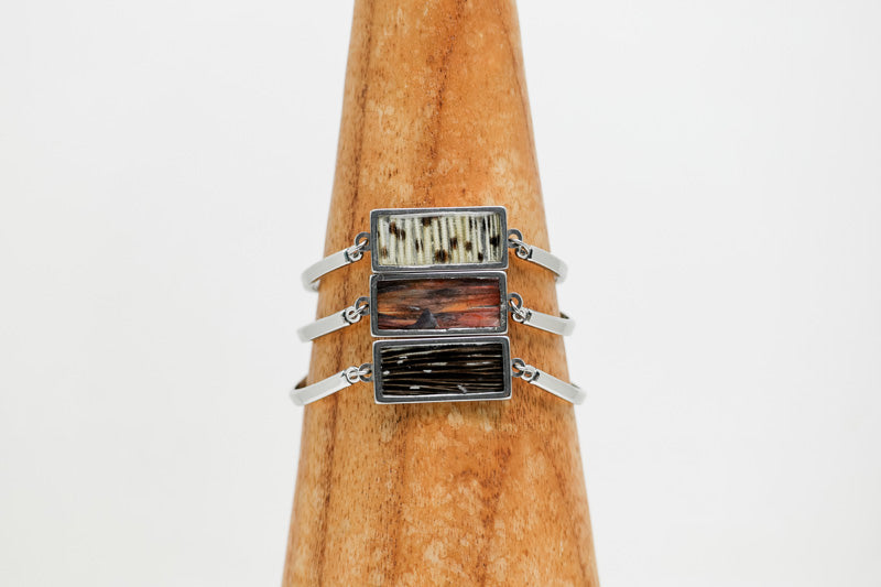 Three silver Bar Bracelets on a wooden triangle on a white background.