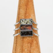 Three silver Bar Bracelets on a wooden triangle on a white background.