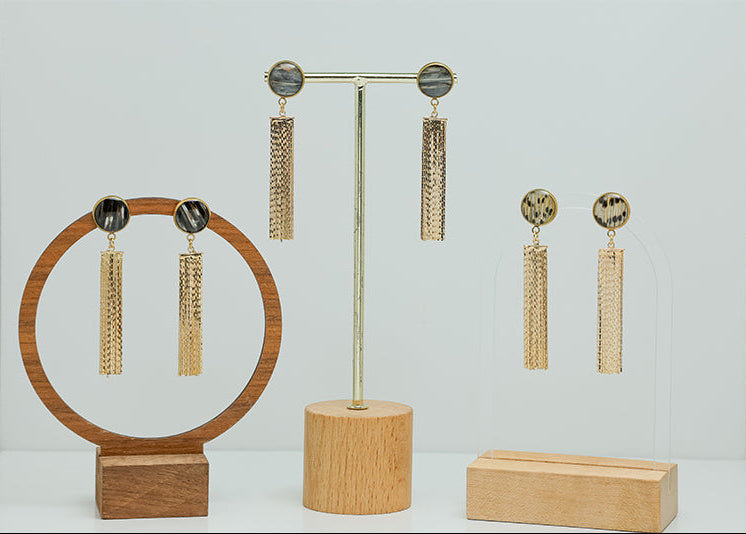 Three pairs of Golden Tassel Earrings on stands on a white background.  
