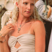 A woman in a cream tube top wearing two bracelets, two necklaces and earrings.