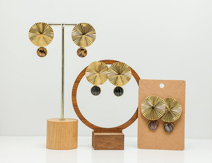 Three pairs of Bold Golden Disc Earrings on stands on a white background.