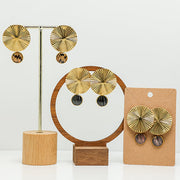 Three pairs of Bold Golden Disc Earrings on stands on a white background.