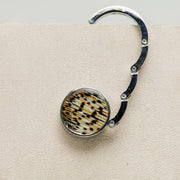 An open Silver Purse Hook Hanger on a cream block.