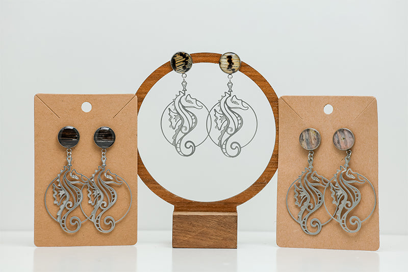 Three pairs of Seahorse Earrings on stands on a white background.  