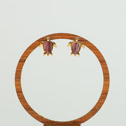 Mini Gold Turtle earrings on a circular wooden stand on a white background.  