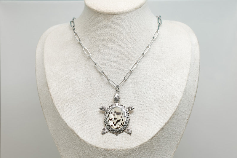 A Turtle Necklace on a cream necklace display bust. 