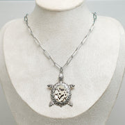 A Turtle Necklace on a cream necklace display bust. 