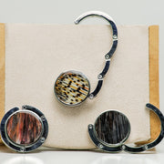 Three silver Purse Hook Hangers on a cream block, one is open, one is half open and one is closed. 
