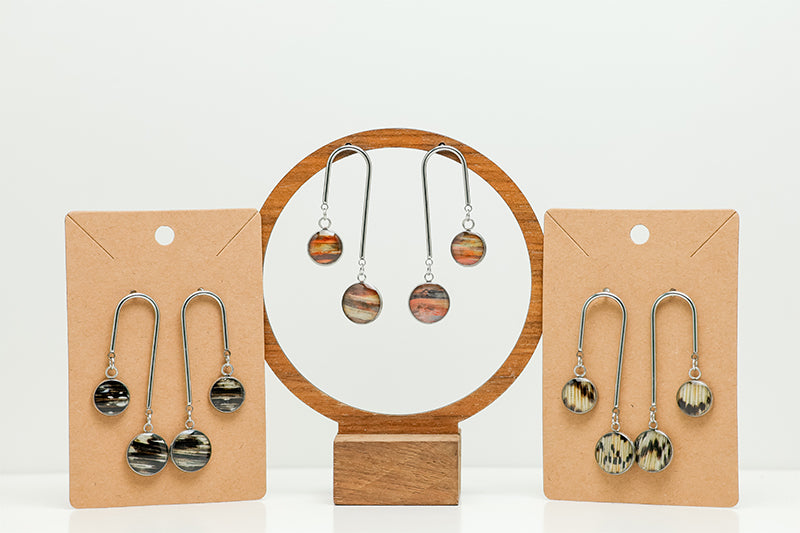Three pairs of Asymmetrical Bar Earrings on stands on a white background.  