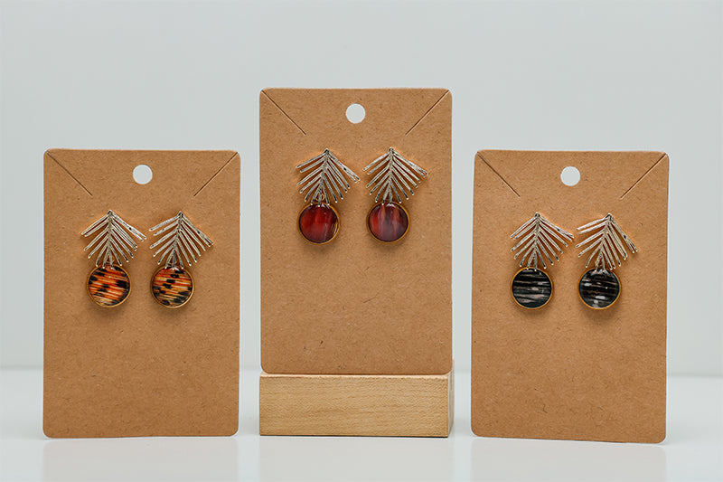 Three pairs of Golden Palm Earrings on cardboard stands on a white background.