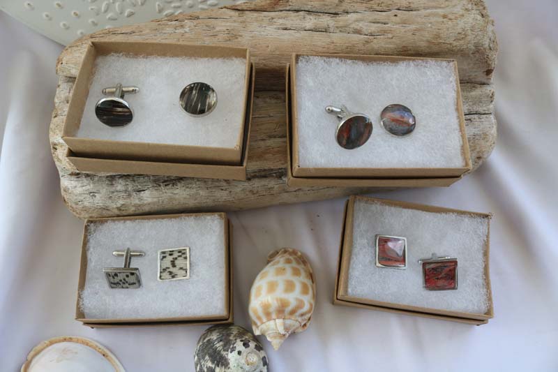 Four jewelry boxes with either a Round Cuff Links in the top row andSquare Cuffs in the bottom row. Link set in the box on a piece of wood on a white tablecloth with three shells on a white tablecloth.