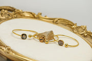 Three gold cuff bracelets with lionfish fin resin pendants in tail, pectoral, and pelvic fin variants displayed on ornate gold decorative tray 