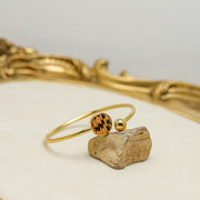 Gold cuff bracelet with lionfish tail fin resin pendant and gold ball end displayed on natural stone within ornate gold decorative tray