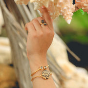 Gold paperclip bracelet with lionfish pendant, gold double pendant bracelet with two lionfish fin resin charms and gold double pendant ring worn on a wrist and hand with coastal shells and greenery background