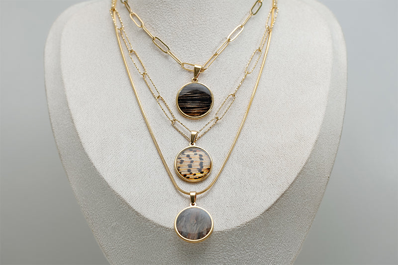 Large gold layered necklace with three lionfish fin resin pendants on paperclip and dainty chain styles displayed on white jewelry bust