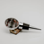 Silver wine bottle stopper with round lionfish pectoral fin resin charm in red and grey streaked pattern displayed on natural stone on white background