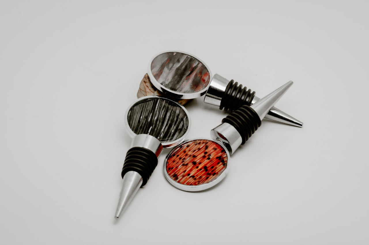 Three silver lionfish fin wine bottle stoppers with round resin charms in tail, pectoral, and pelvic fin variants displayed together on white background
