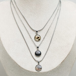 Three silver necklaces with lionfish pendants on a white mannequin bust.